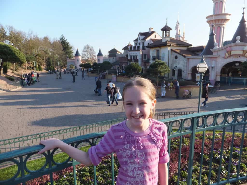 Young girl in purple shirt standing by fence in Disneyland Paris.