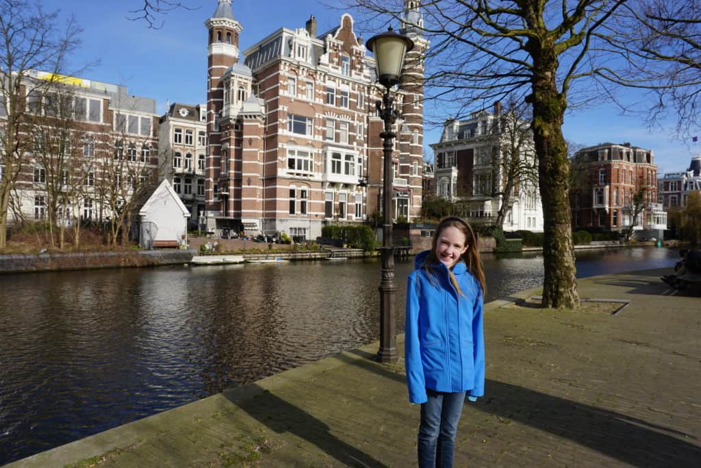 Young girl in blue coat by canal in Amsterdam.