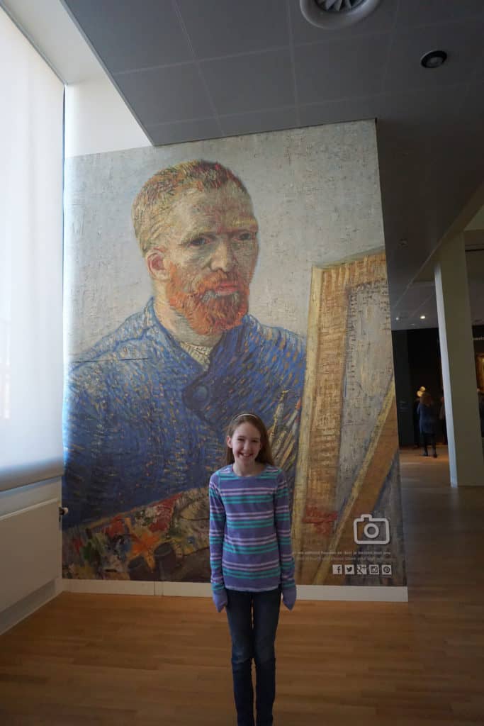 Young girl standing in front of poster of Van Gogh painting at Van Gogh Museum in Amsterdam.