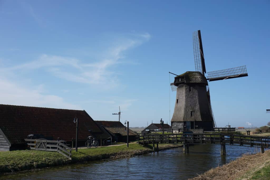 A windmill and additional buildings sitting alongside a canal in Dutch countryside.