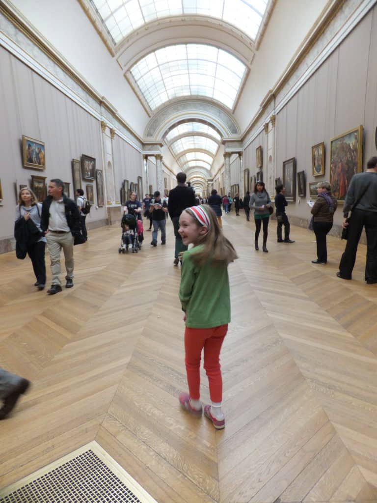 Young girl in green shirt looking back as she walks through hallways of the Louvre Museum in Paris, France.