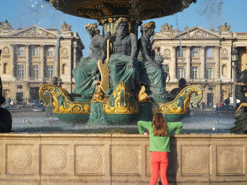 Young girl in orange pants and green shirt looking at the fountain in Place de la Concorde in Paris. 