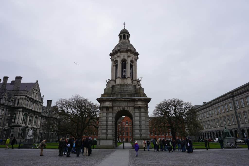 Groups of people standing around tower at entrance to Trinity College, Dublin.