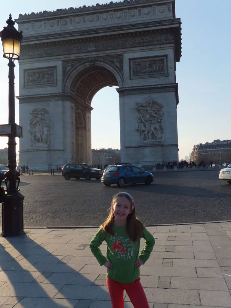 Young girl in green shirt posing with hands on hips in front of the Arc de Triomphe in Paris, France.