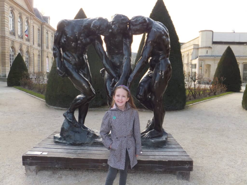 Young girl in front of Three Shades sculpture in the gardens at Musee Rodin in Paris.