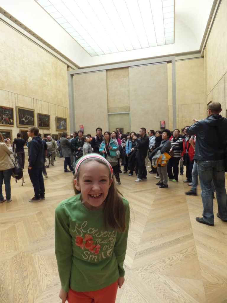 Young grinning girl in green shirt in the crowded room at the Louvre in Paris where the Mona Lisa is on display.
