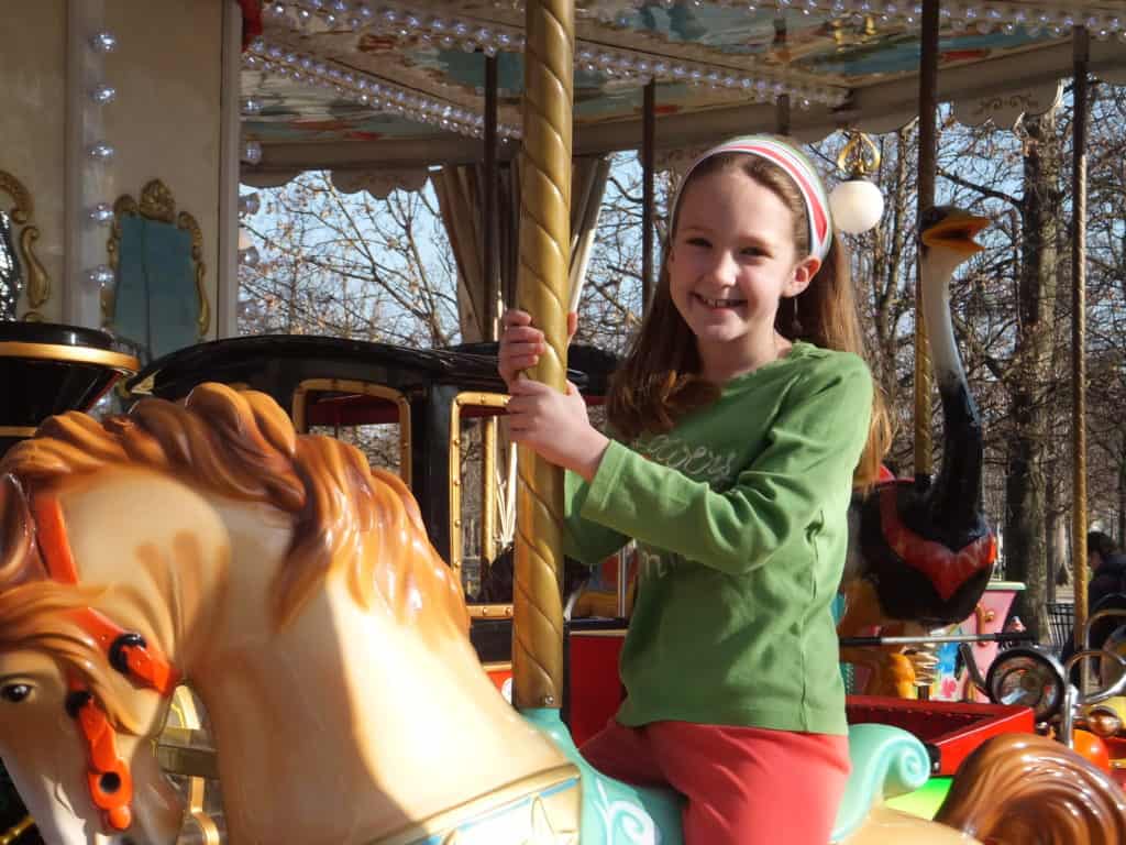 Young girl in green shirt smiling as she rides carousel in Tuileries Gardens in Paris.