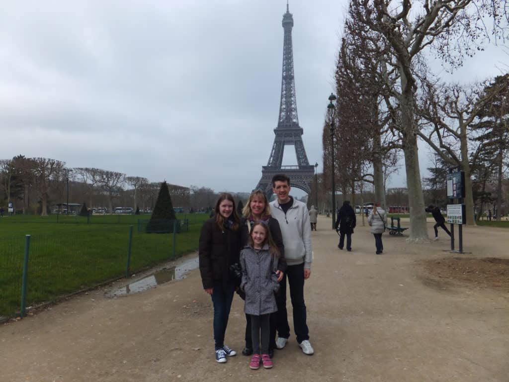 Dad, mom and two daughters standing in front of Eiffel Tower in Paris on an overcast spring day.