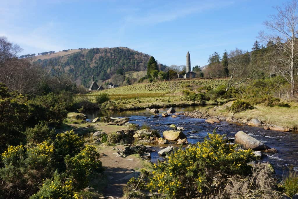 Small stream surrounded by bushes with Round Tower of Monastic City in background, Glendalough, Ireland.