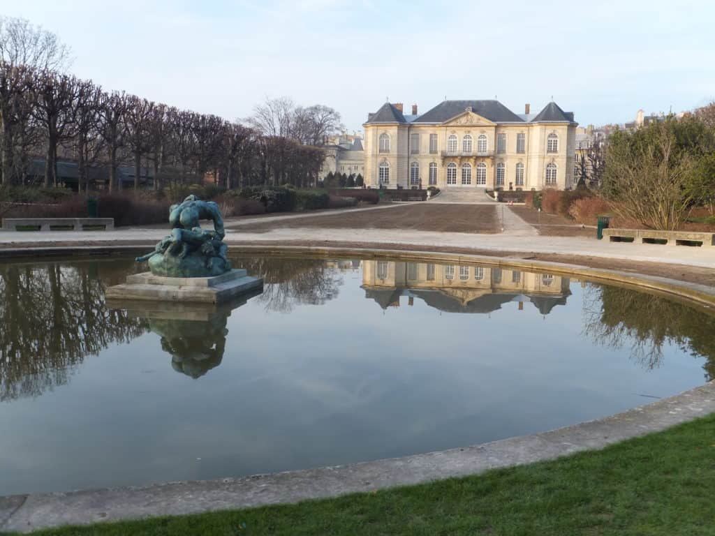 Museum and gardens at Musee Rodin in Paris reflected in pool of water with sculpture.