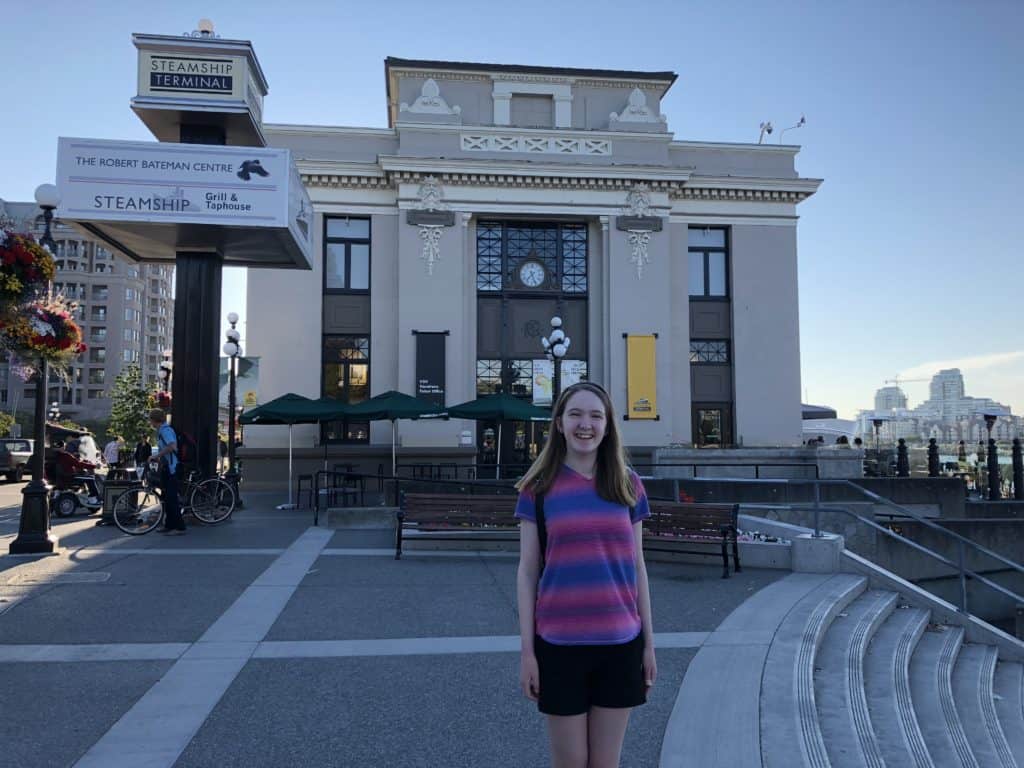 Teen girl standing outside Steamship Terminal with green Starbucks umbrellas in background in Victoria, BC.