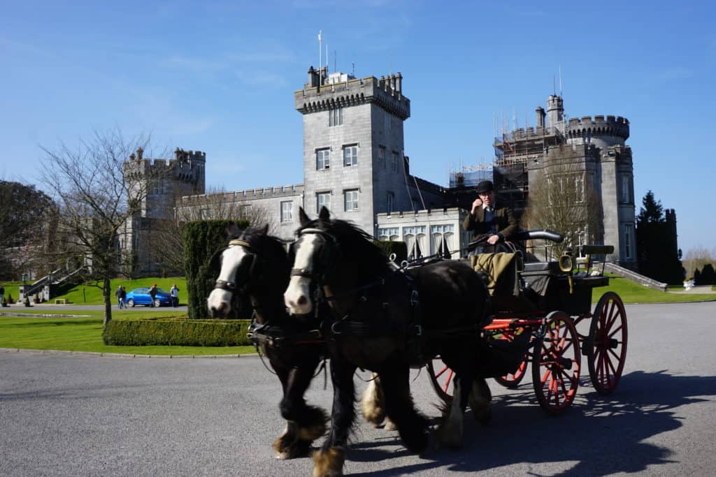 Man riding in cart pulled by two horses with Dromoland Castle in background.