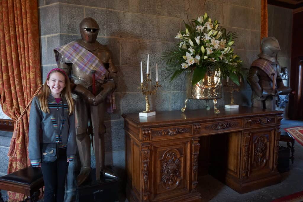 Young girl standing beside a suit of armour and an elaborate wooden desk with candles and flowers displayed on top in lobby of Dromoland Castle in Ireland.