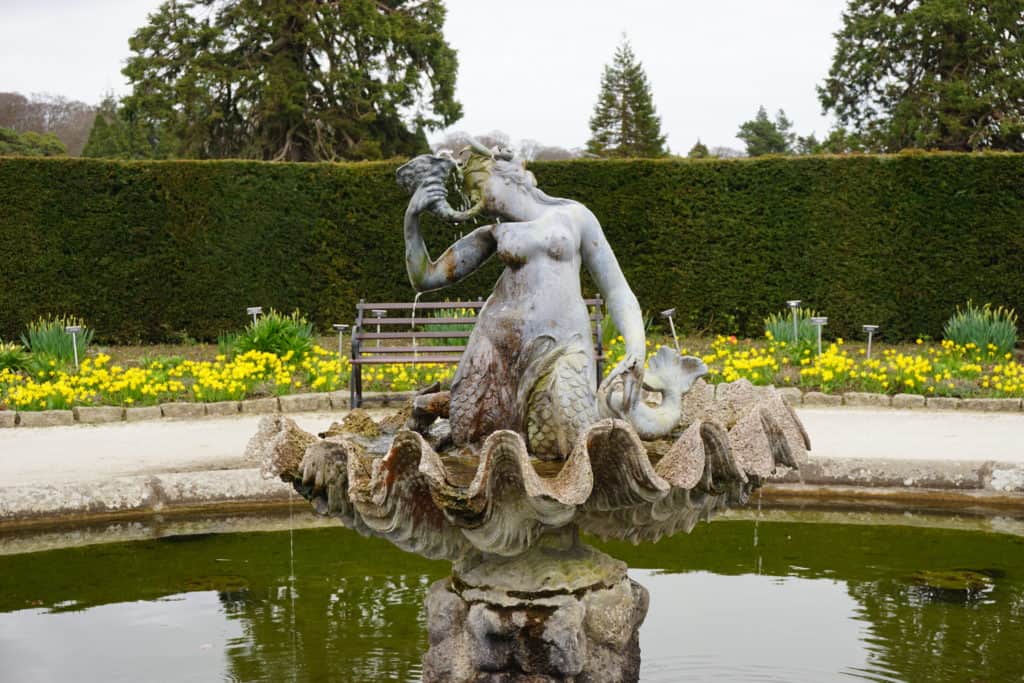 Sculpture in fountain at Powerscourt Gardens in Ireland - yellow flowers and garden hedge in background.