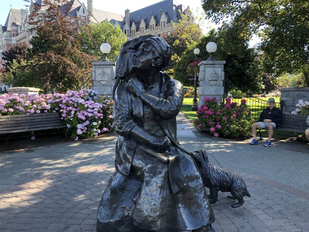 Sculpture of Emily Carr in Victoria, British Columbia with flowers and benches in background and gate to the Fairmont Empress.