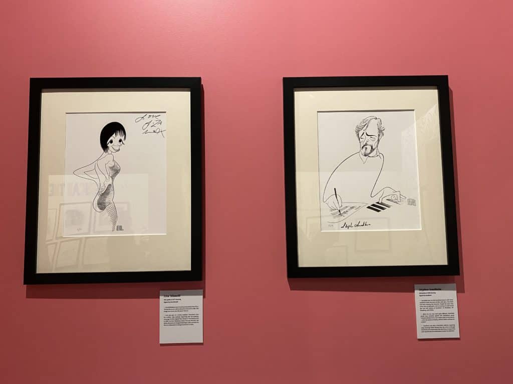Hirschfeld sketches of Liza Minnelli and Stephen Sondheim in black frames displayed on red wall at Museum of Broadway in New York City.