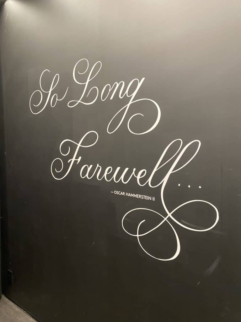 Black wall with painted words - So Long Farewell in cursive and underneath - Oscar Hammerstein II.