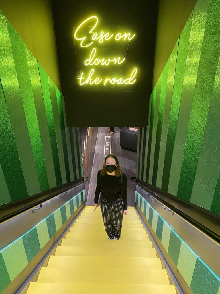 Looking down staircase to young woman standing on yellow stairs and walls painted green stripes