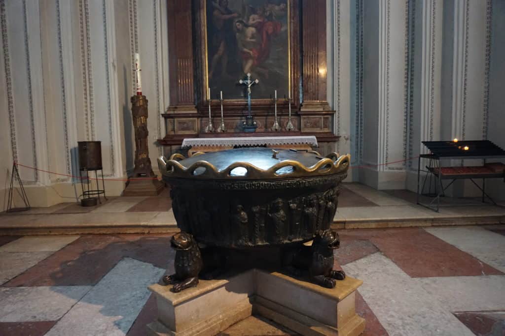 Baptismal font with painting hanging on wall in background at Salzburg Cathedral.