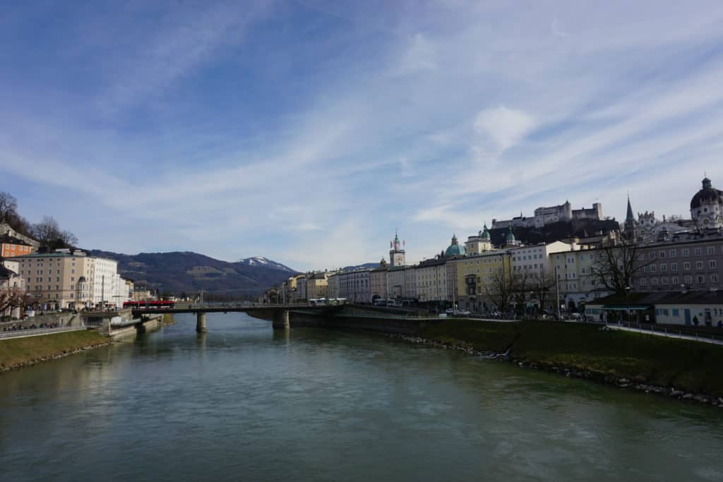 Buildings on either side of river in Salzburg, Austria and mountains in the background.
