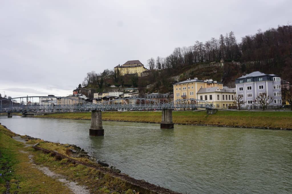 Footbridge across river with buildings on the other side and hills in background in Salzburg, Austria.