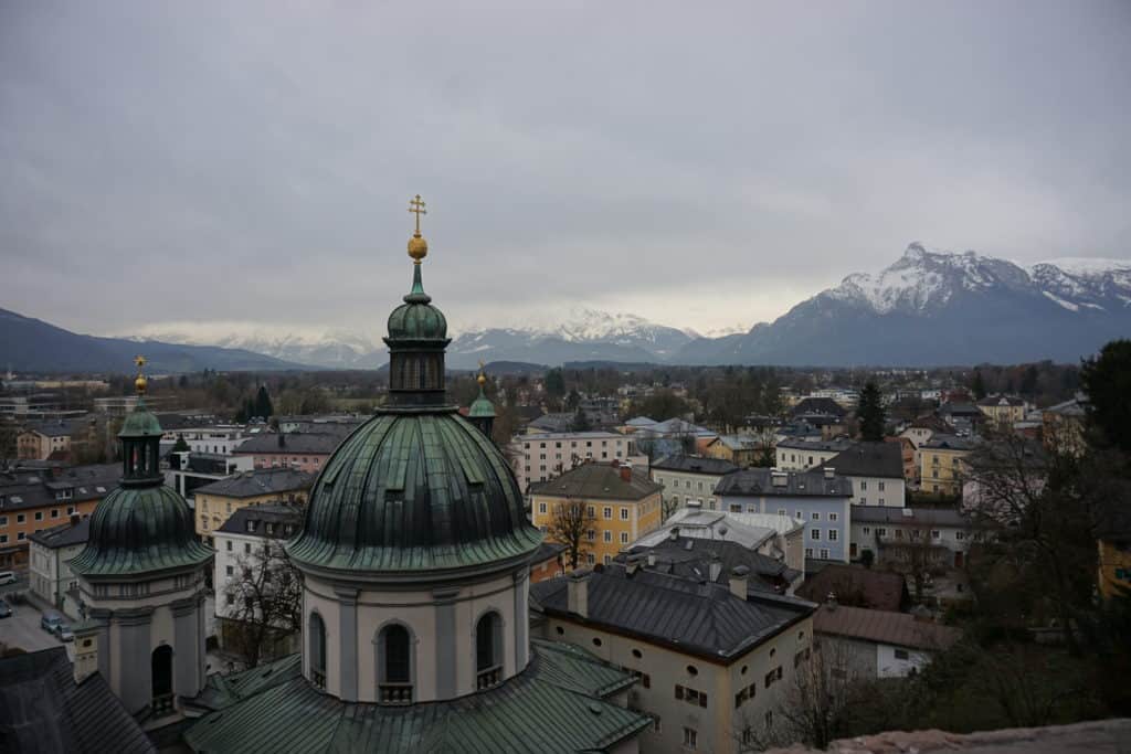 View of rooftops, domed church and snow-topped mountains in Salzburg, Austria.