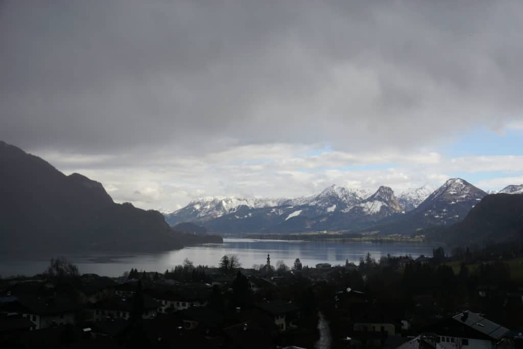 Snow-capped mountains behind lake on mostly overcast day in Salzburg Lake District.