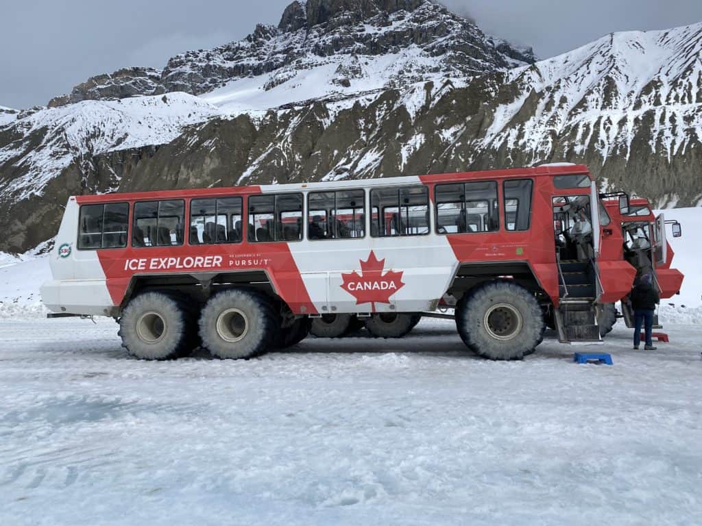 Large red and white Ice Explorer vehicle on Athabasca Glacier with mountains in background.
