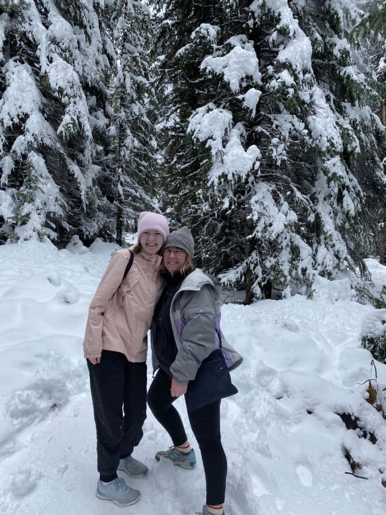 Two women at Peyto Lake standing in snow in front of snow-covered trees.