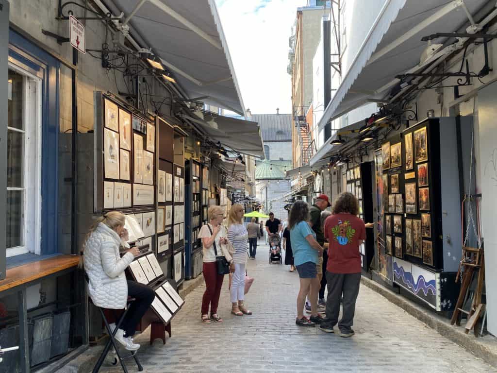 People looking at artwork displayed along the walls of Rue du Tresor in Quebec City.