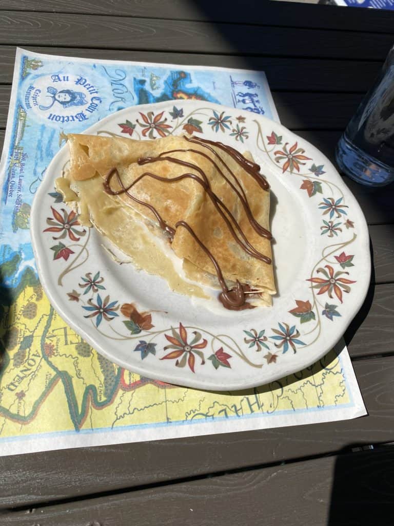 Crepe with caramel sauce drizzled on top sitting on a white plate decorated with flowers on rim.