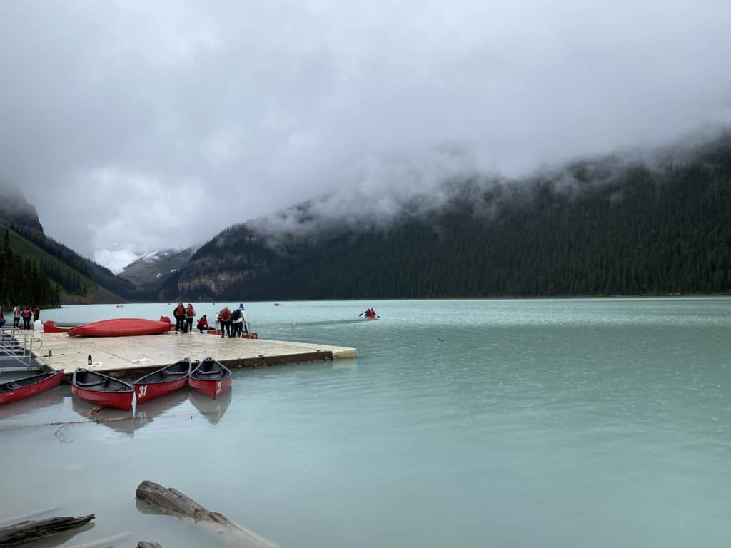 Foggy day at Lake Louise in Banff National Park, Alberta - people standing on platform with red canoes.