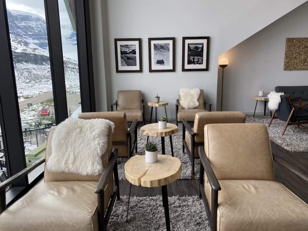 Seating area in Glacier View Lodge lobby - brown leather chairs, photos on wall alongside window looking out at Columbia Icefields.