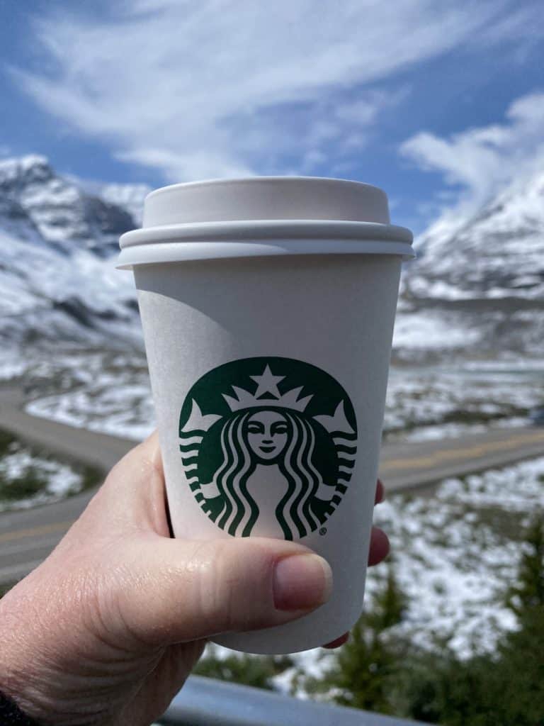 Starbucks cup held up with background of blue sky, snow-capped mountains of Columbia Icefield.