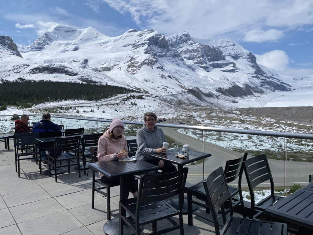 People dining on outdoor terrace at Glacier View Lodge with Columbia Icefields in background.