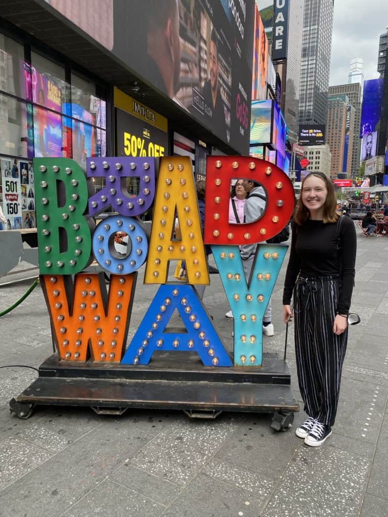 Young woman standing beside multi-coloured Broadway sign.