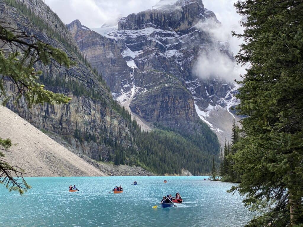 Several canoes paddling on bright blue Moraine Lake with snow-capped mountains in background.