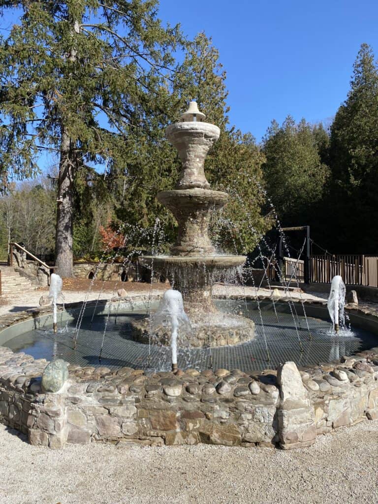 Antique fountain at Belfountain Conservation Area with evergreen trees in background.