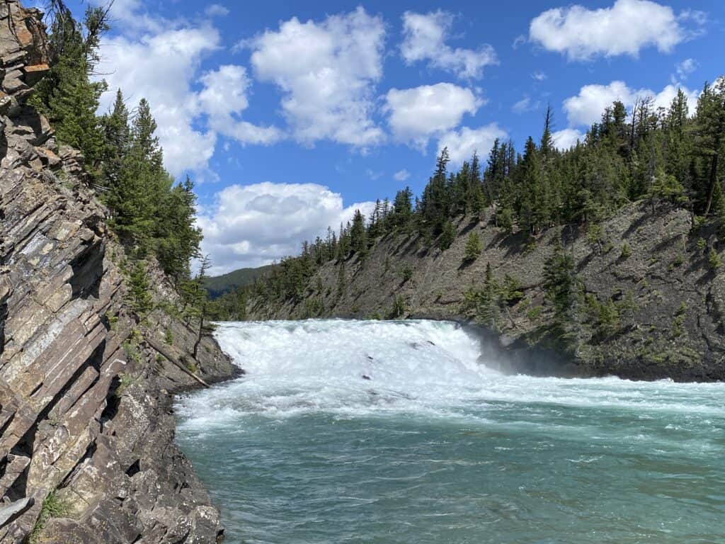 Bow Falls in Banff, Alberta with blue sky and fluffy white clouds.