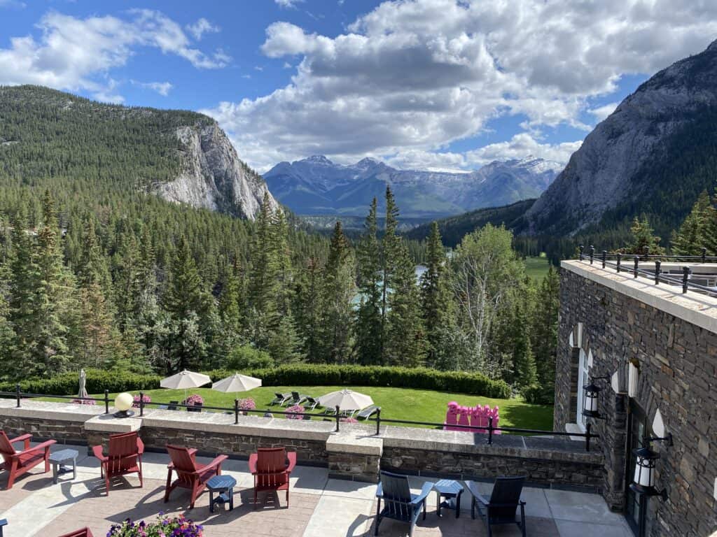 Seating area at back of Fairmont Banff Springs hotel with chairs and umbrellas - view of mountains on beautiful early summer day.