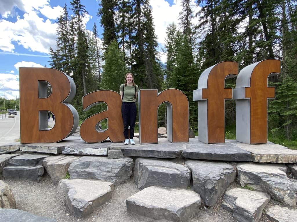 Young woman in green shirt and black pants posing in front of the Banff sign.