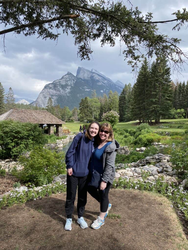 Two women standing in Cascade Gardens, Banff with gardens and mountains in the background.