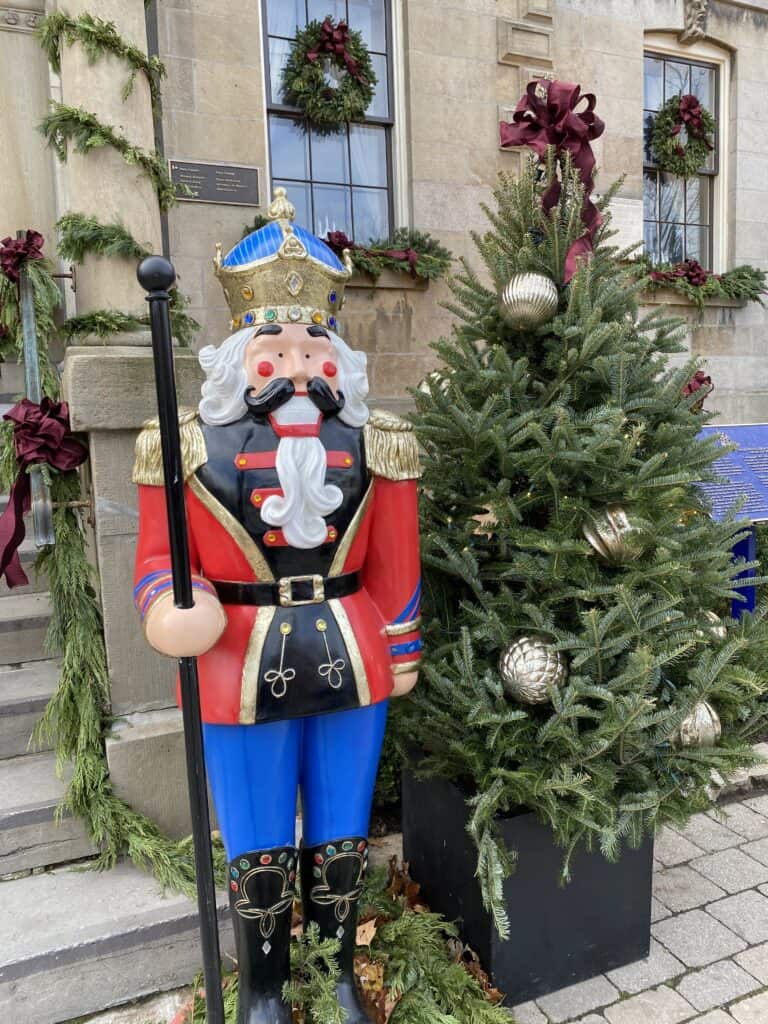 Decorated Christmas tree and red and blue holiday soldier decoration in front of old courthouse building decorated with greenery and burgundy bows in Niagara-on-the-Lake
