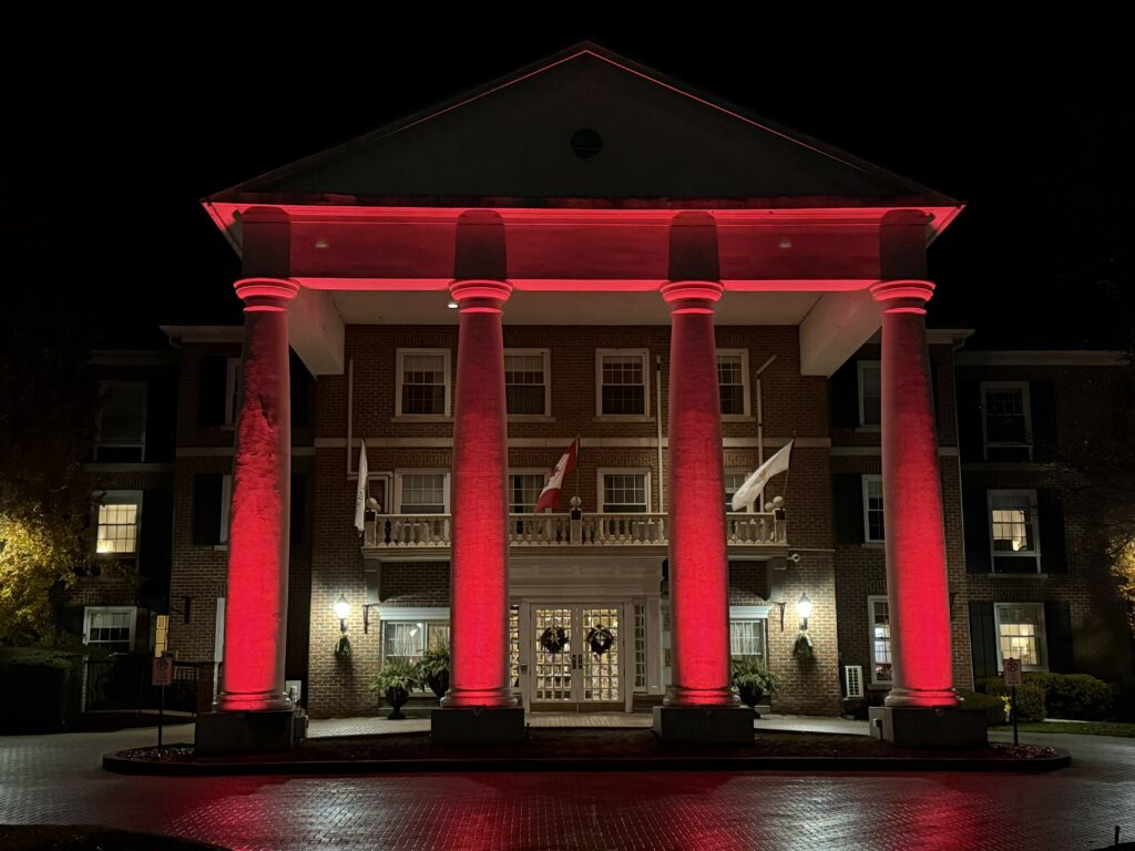 exterior of Queen's Landing hotel at night during the holiday season with columns at front of building lit red and wreaths on front entrance doors.
