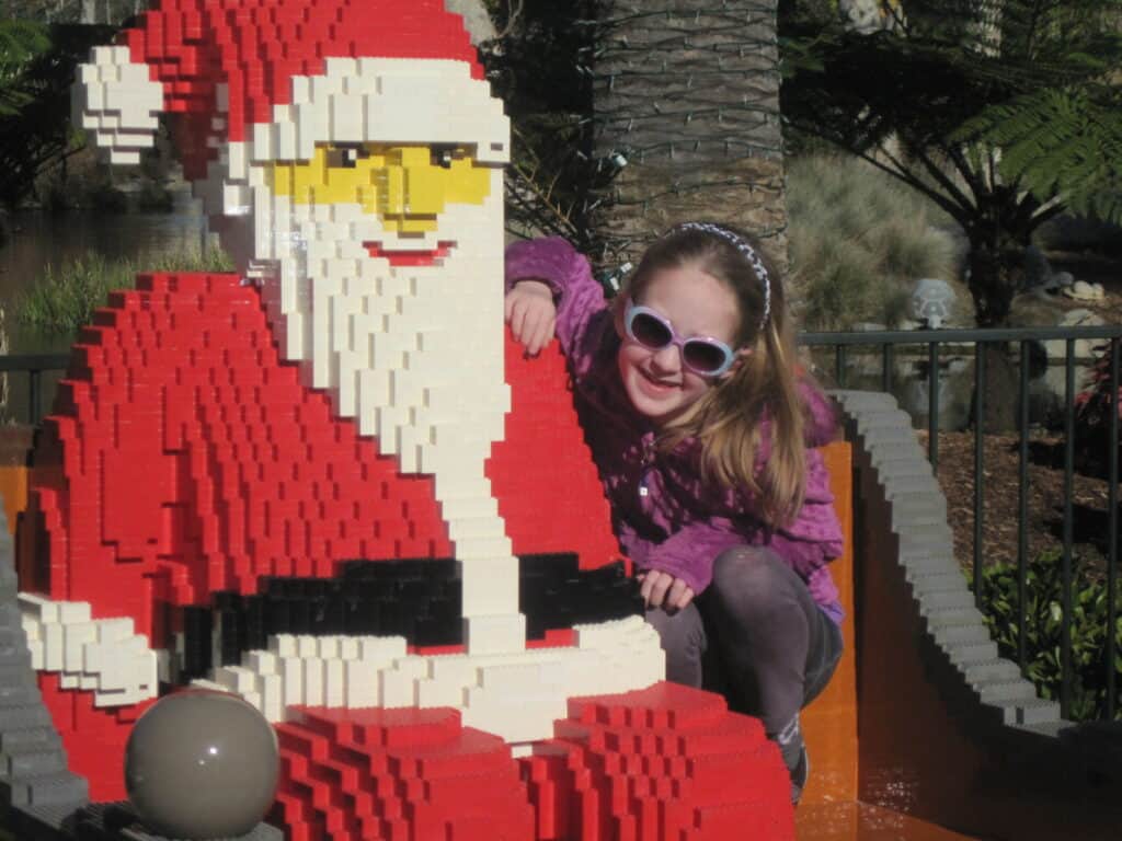Young girl wearing sunglasses sitting with LEGO Santa at LEGOLAND California.