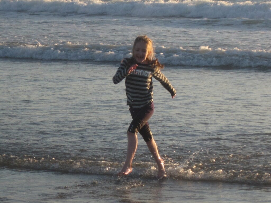 Young girl in striped shirt playing in the surf on the beach at Hotel del Coronado in San Diego during the Christmas holidays.