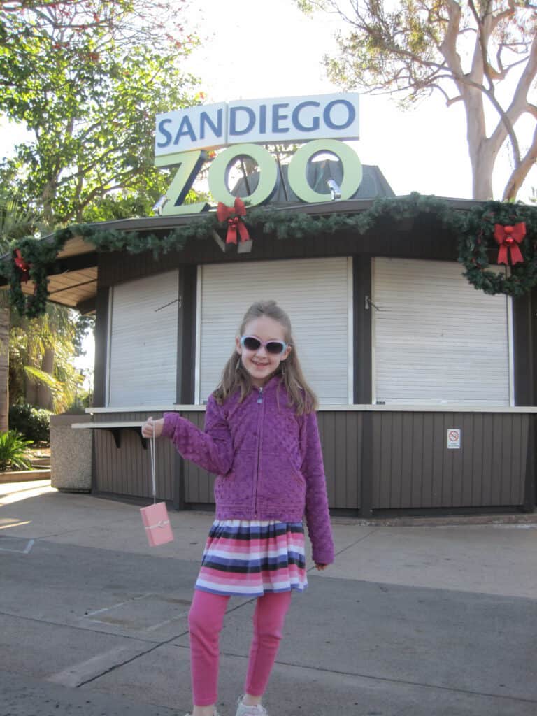 Young girl standing at entrance to San Diego Zoo decorated for Christmas season.