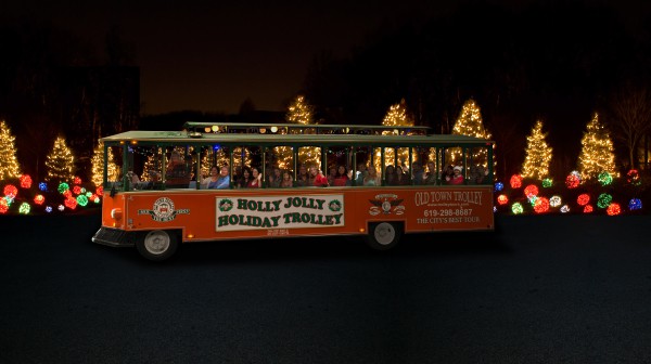 Holly Jolly Holiday Trolley car at night in front of Christmas trees and lights.