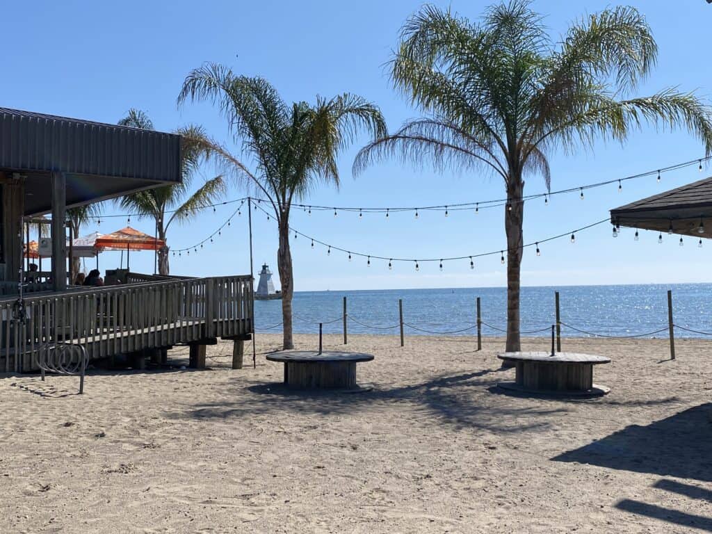 Restaurant patio and palm trees on beach with lighthouse in background in Port Dover, Ontario.