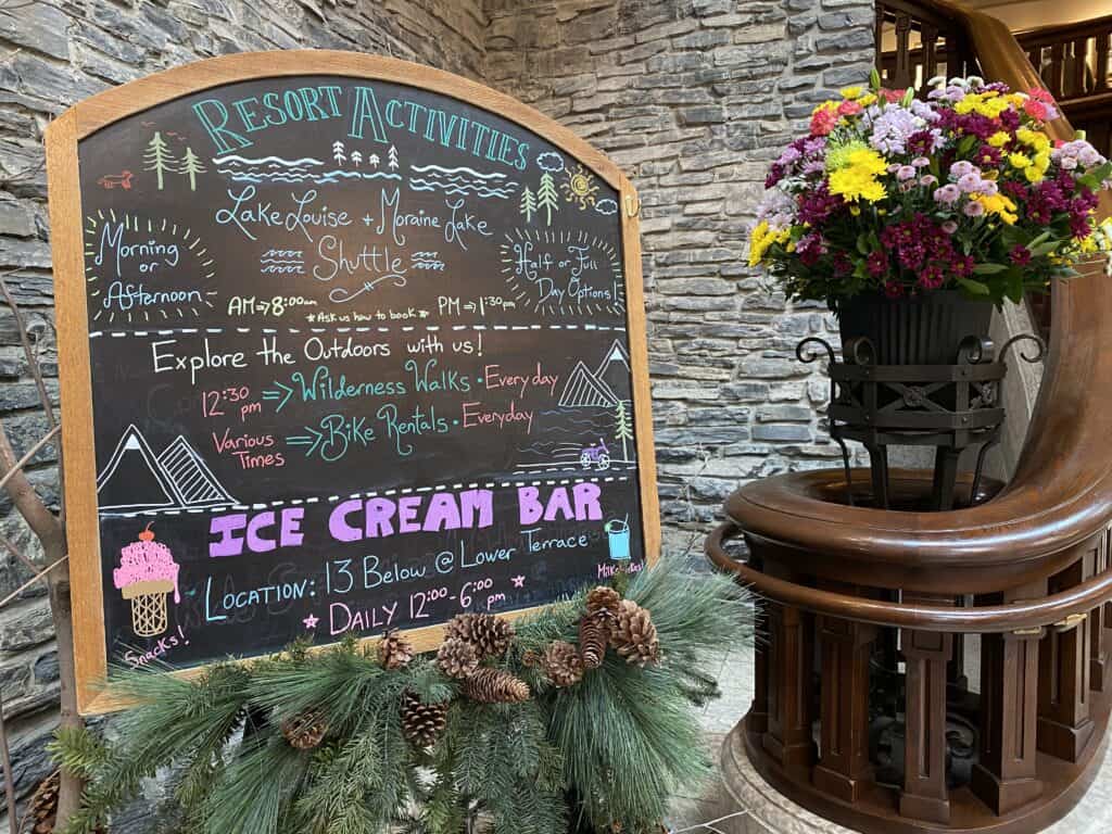 Chalkboard listing Resort Activities at bottom of staircase next to flower arrangement in lobby of the Fairmont Banff Springs Hotel.
